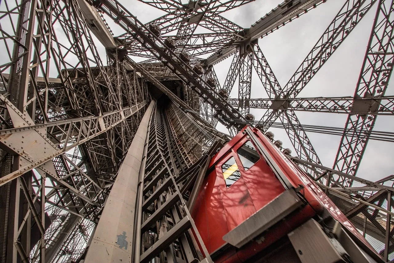 Una cabina roja de ascensor subiendo por la estructura de hierro de la torre