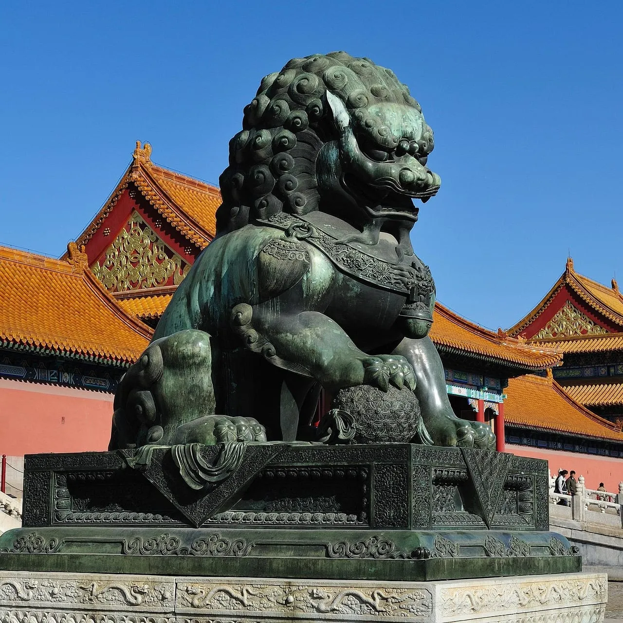 Un león guardián de bronce delante de muros rojos y tejados amarillos