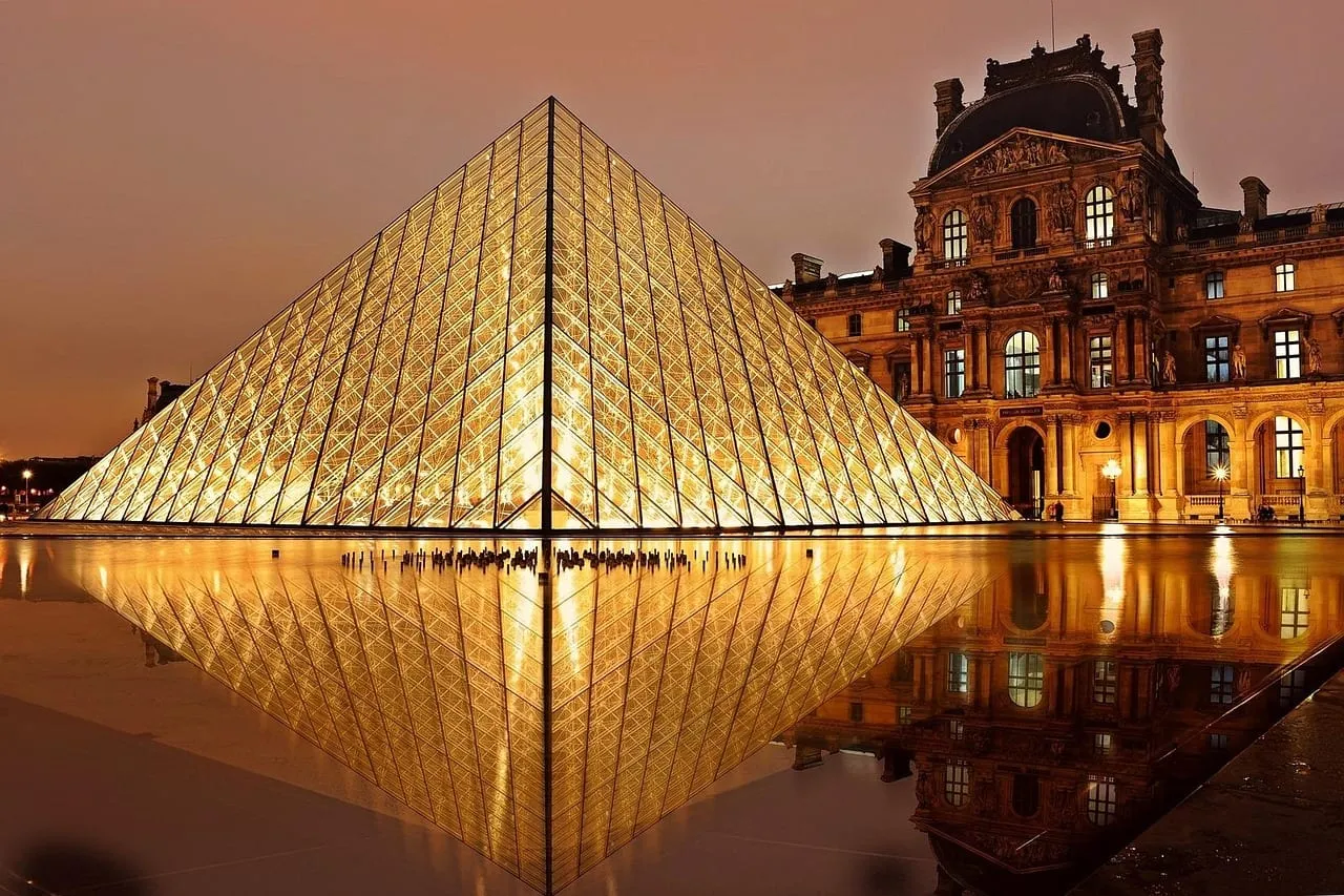 La pirámide del Louvre iluminada al anochecer, reflejada en los estanques