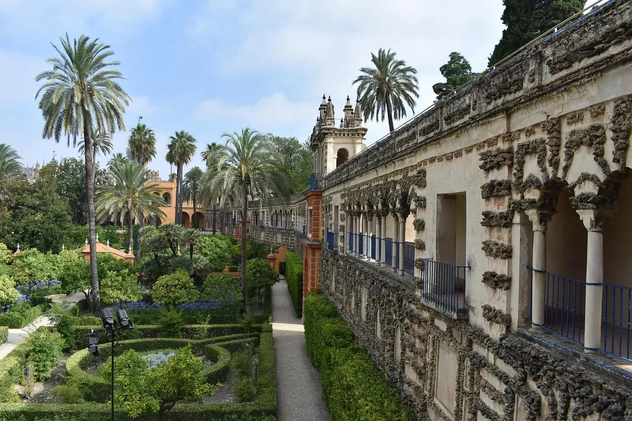 Palmeras y jardines con setos de boj junto a una galería con arcadas